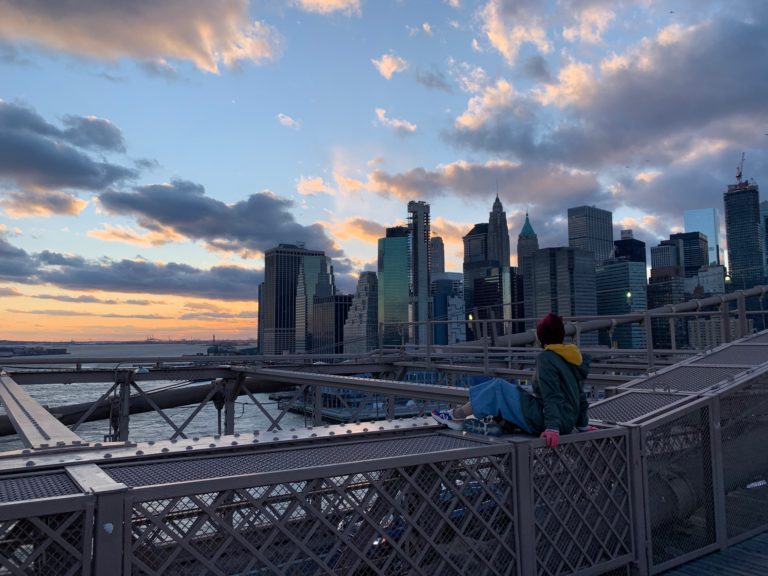 ragazza seduta su ponte di Brooklyn al tramonto